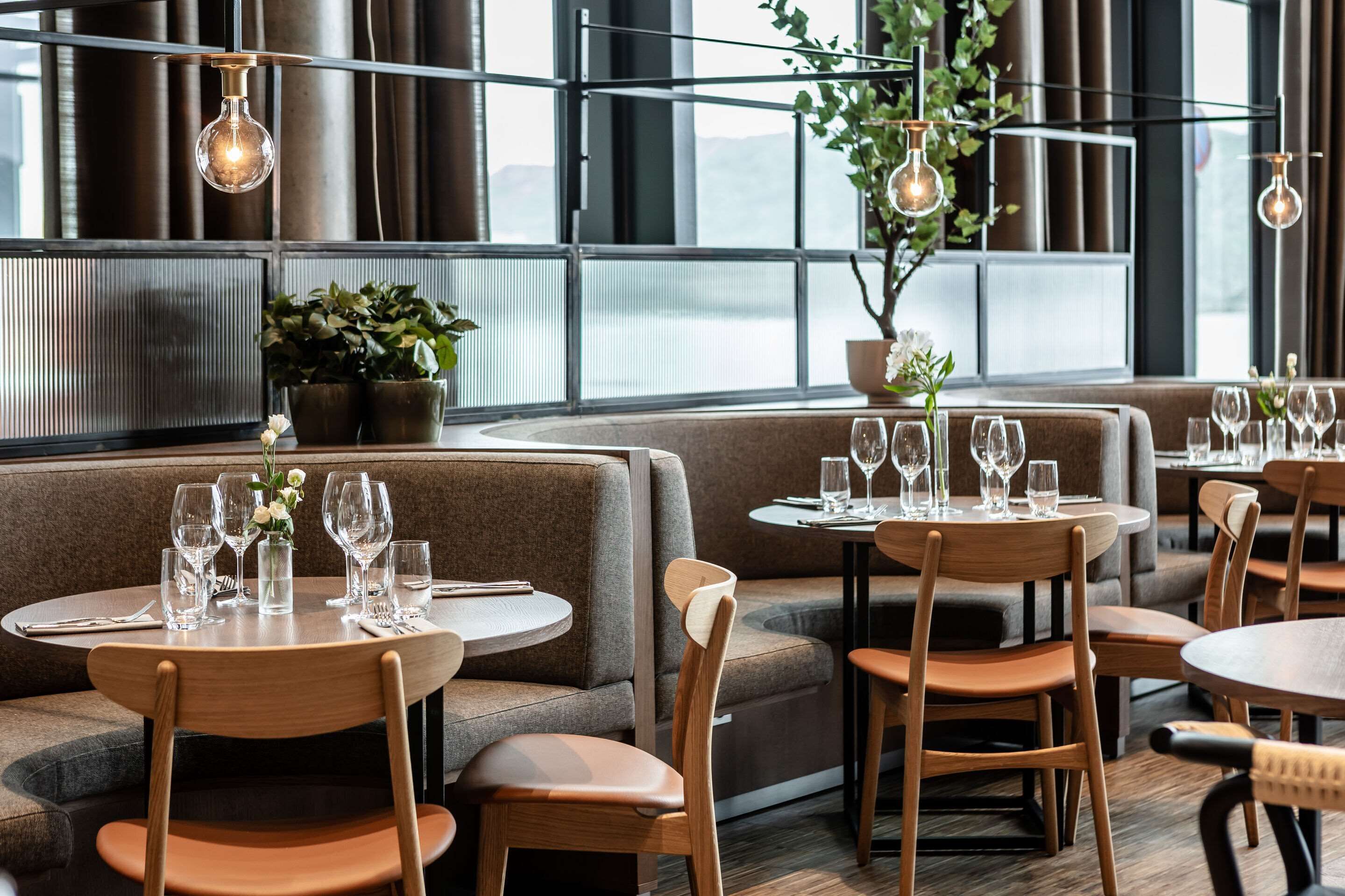 A restaurant with round tables, wooden chairs, and a large window with a view.