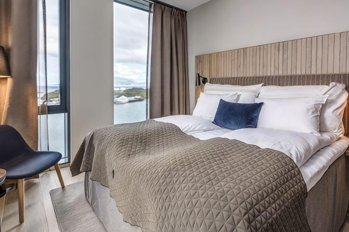 Ett modernt hotellrum med en stor säng, utsikt över vattnet och en sänggavel i trä.