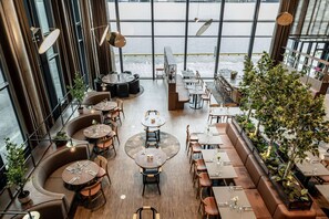 A modern restaurant with round tables and booths, large windows overlooking a body of water, and indoor plants. - Quality Hotel Ramsalt (Bodo)