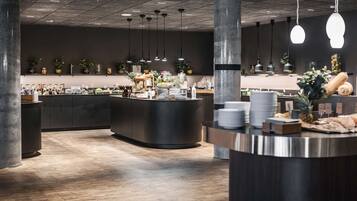 Een modern restaurant met een centrale balie, hangende lampen en potplanten.