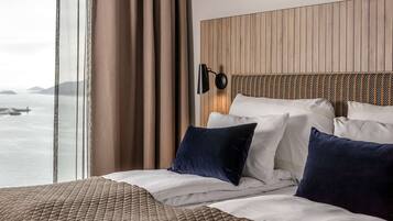 Habitación de hotel con una cama grande, cabecera con diseño de panel de madera, lámpara fijada a la pared y vistas al mar.