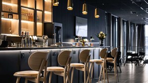 A modern bar area with wooden bar stools, a counter with bar tools, and a large window in the background. - Quality Hotel Ramsalt (Bodo)