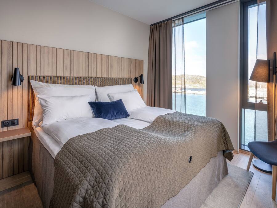 A modern hotel room with a large bed, a view of the sea, and a seating area.