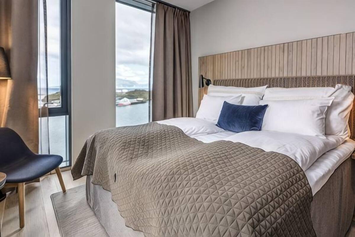 A modern hotel room with a large bed, a view of the water, and a wooden headboard.