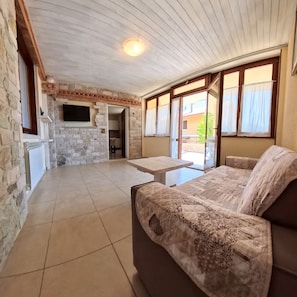 A spacious living area with a stone wall, a flat-screen TV, a sofa, and a dining table.