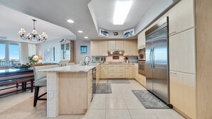 A modern kitchen with a large island, stainless steel appliances, and wooden cabinetry. - DOWN BY THE BAY! 2nd floor unit, AMAZING views! 65”TV! ASK ABOUT DISCOUNTS! (Orange Beach)