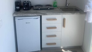 A compact kitchen with white cabinets, a built-in dishwasher, a coffee maker, a kettle, and a sink. - Amazing Studio with Sea view in Mykonos (Mykonos)