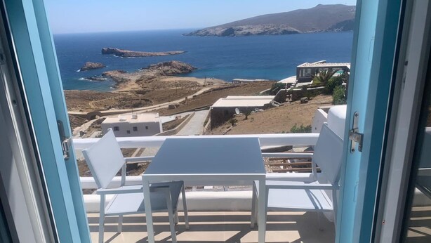 A balcony with a table and chairs overlooking a coastal landscape with rocky terrain and a clear blue sea. - Amazing Studio with Sea view in Mykonos (Mykonos)