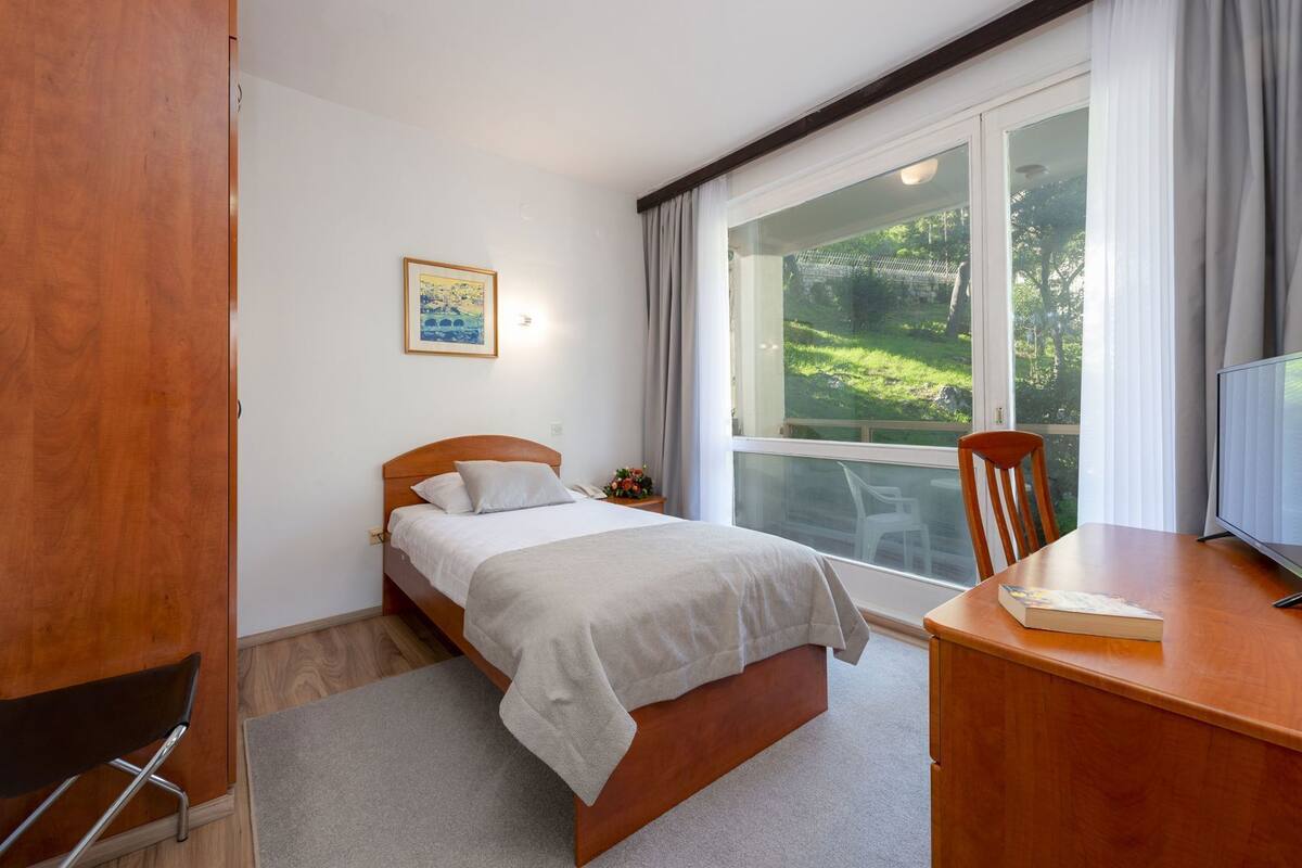 A bedroom with a bed, a desk, a chair, a window, and a painting on the wall.