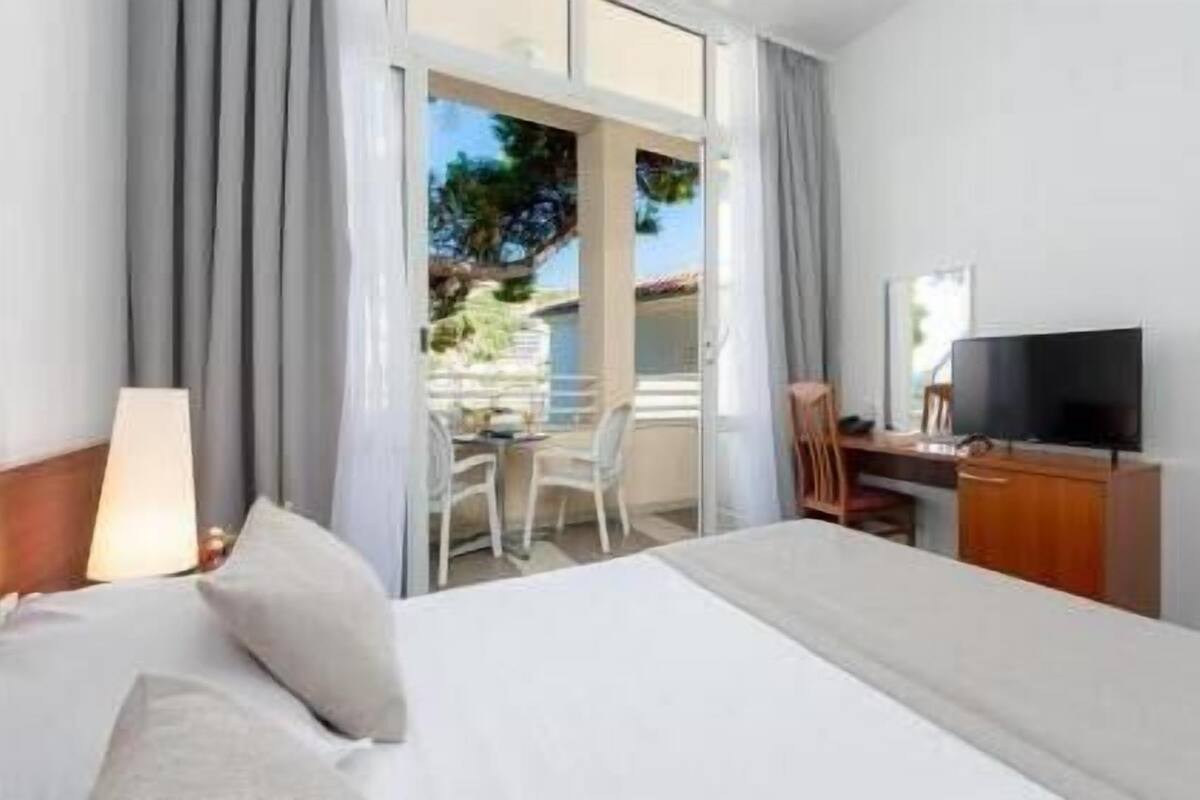 A hotel room with a bed, a desk, a chair, a TV, and a balcony with a view.