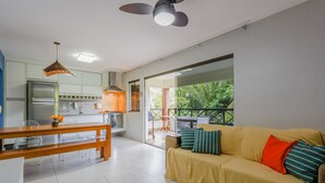 Une cuisine moderne avec un coin repas, un canapé agrémenté de coussins et un balcon offrant une vue sur la verdure.