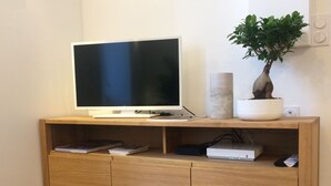 A wooden entertainment center with a flat-screen TV, a plant, and a gaming console.