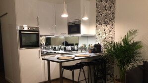 A modern kitchen with white cabinets, stainless steel appliances, a central island with stools, and a patterned wallpaper.