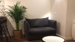 A living room with a dark grey sofa, a round black coffee table, a woven plant pot, and a patterned wall.