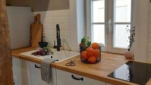 A kitchen with white cabinets, a wooden countertop, a black induction cooktop, a window with white frames, and a bowl of oranges on the counter. - Modern vacation apartment "Lamm" 2 - 3 persons  (Sinsheim)
