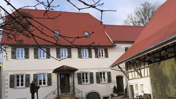 A traditional building with a red-tiled roof, multiple windows with shutters, and a cobblestone courtyard. - Modern vacation apartment "Lamm" 2 - 3 persons  (Sinsheim)