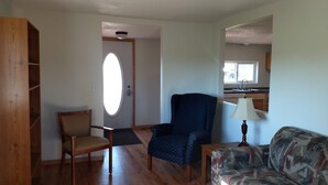 A living room with a wooden bookshelf, a blue armchair, a patterned sofa, and a lamp. - The Red House (Rapid City)