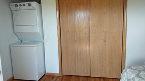 A laundry room with stacked washers and dryers, a wooden wardrobe, and a patterned bed. - The Red House (Rapid City)