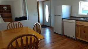 A kitchen with wooden cabinets, a white refrigerator, a dishwasher, and a dining table with chairs. - The Red House (Rapid City)