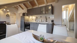 Una cocina moderna con armarios grises, un refrigerador de acero inoxidable y una zona de comedor con una mesa y sillas blancas.
