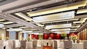 Une salle de banquet avec des tables rondes, des chaises et des centres de table floraux.