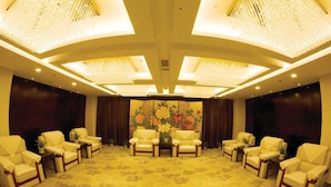 Une salle de conférence dotée d’un tapis à motifs floraux, de chaises blanches et d’un grand tableau au fond.