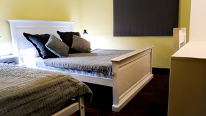 Ein Schlafzimmer mit zwei Einzelbetten, einem Nachttisch mit Lampe und einem an der Wand befestigten Fernseher.