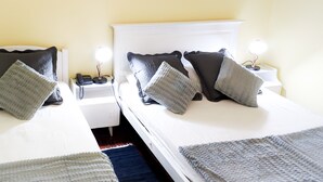Ein Hotelzimmer mit zwei Betten, jeweils mit weißem Kopfteil, grau-schwarzen Kissen und Nachttischlampen.