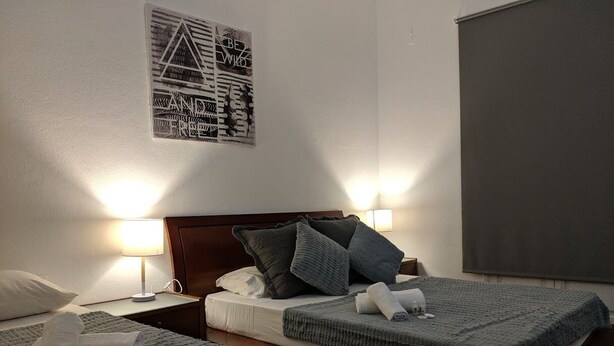 Ein Hotelzimmer mit zwei Betten, jeweils mit grauer Decke und Kissen, einem Holzkopfstück und einer wandmontierten Lampe.