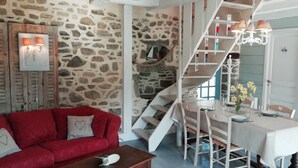 A cozy living room with a red sofa, a wooden coffee table, and a staircase leading to a dining area with a table set for two.