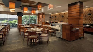 Ein Restaurant mit Holztischen, einem großen Fernseher und Blick ins Grüne.