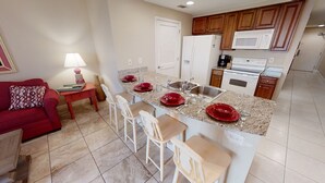 Una cocina compacta con una isla central, una zona de comedor con un sofá rojo y una mesita con una lámpara.
