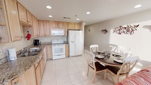 A kitchen with wooden cabinets, a white refrigerator, a stove, and a dining table with chairs. - Splash 606W Master Gulf View Free Beach Service, Golf & Activities Daily (Panama City Beach)