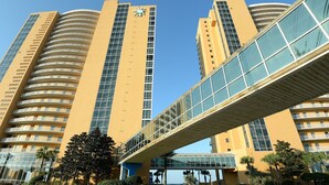 A modern high-rise building with a curved facade, a pedestrian bridge, and a clear blue sky. - Splash 606W Master Gulf View Free Beach Service, Golf & Activities Daily (Panama City Beach)