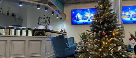 Zona de recepción con un árbol de Navidad, una silla azul y un televisor mostrando un paisaje nevado.
