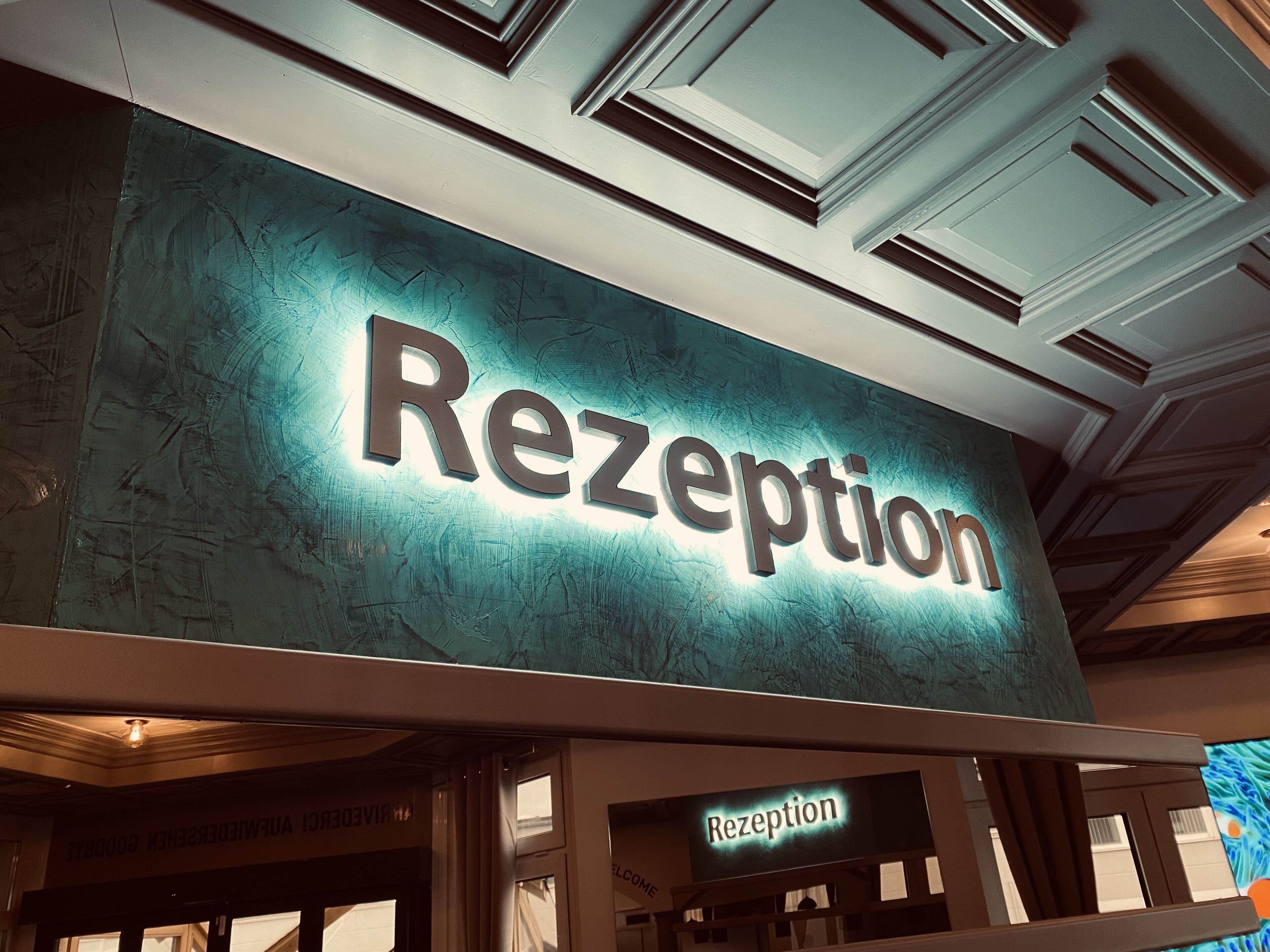 Ein Empfangsbereich mit einem Schild, auf dem 'Rezeption' steht, und einem kleineren Schild darunter mit der Aufschrift 'Rezeption'.