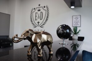 A gold elephant figurine on a reflective surface, with a logo and text on the wall behind it. - E&D Hotel (Rodgau)