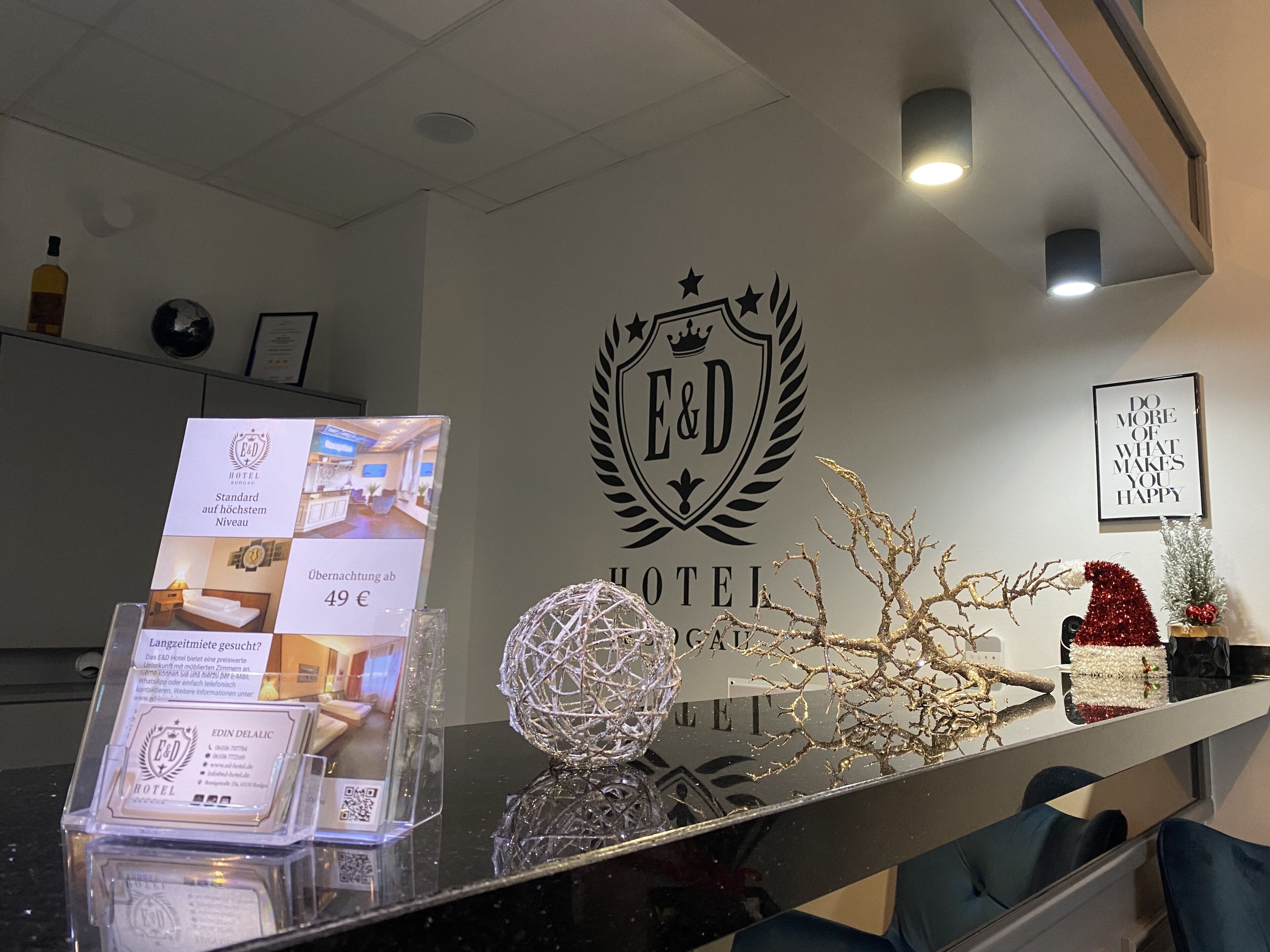 Een hotel receptie met een receptiebalie, een decoratieve bol en een wandbordje met de naam en het logo van het hotel.