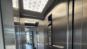 Un ascensor amb interior metàl·lic, un panell de control amb botons i una làmpada de sostre amb disseny.