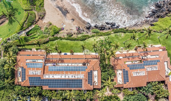 Un resort con varias construcciones que incluyen paneles solares en la azotea, rodeado de abundante vegetación y una playa.