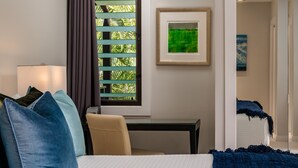 Habitación de hotel con cama, escritorio, ventana con persianas e imagen en un marco en la pared.