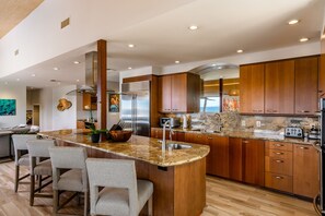 A modern kitchen with granite countertops, stainless steel appliances, wooden cabinets, and a central island with bar stools.