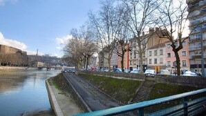 A riverside view with a bridge, buildings, and a pedestrian walkway. - Large studio in Valmy, comfort and calm guaranteed (Lyon)