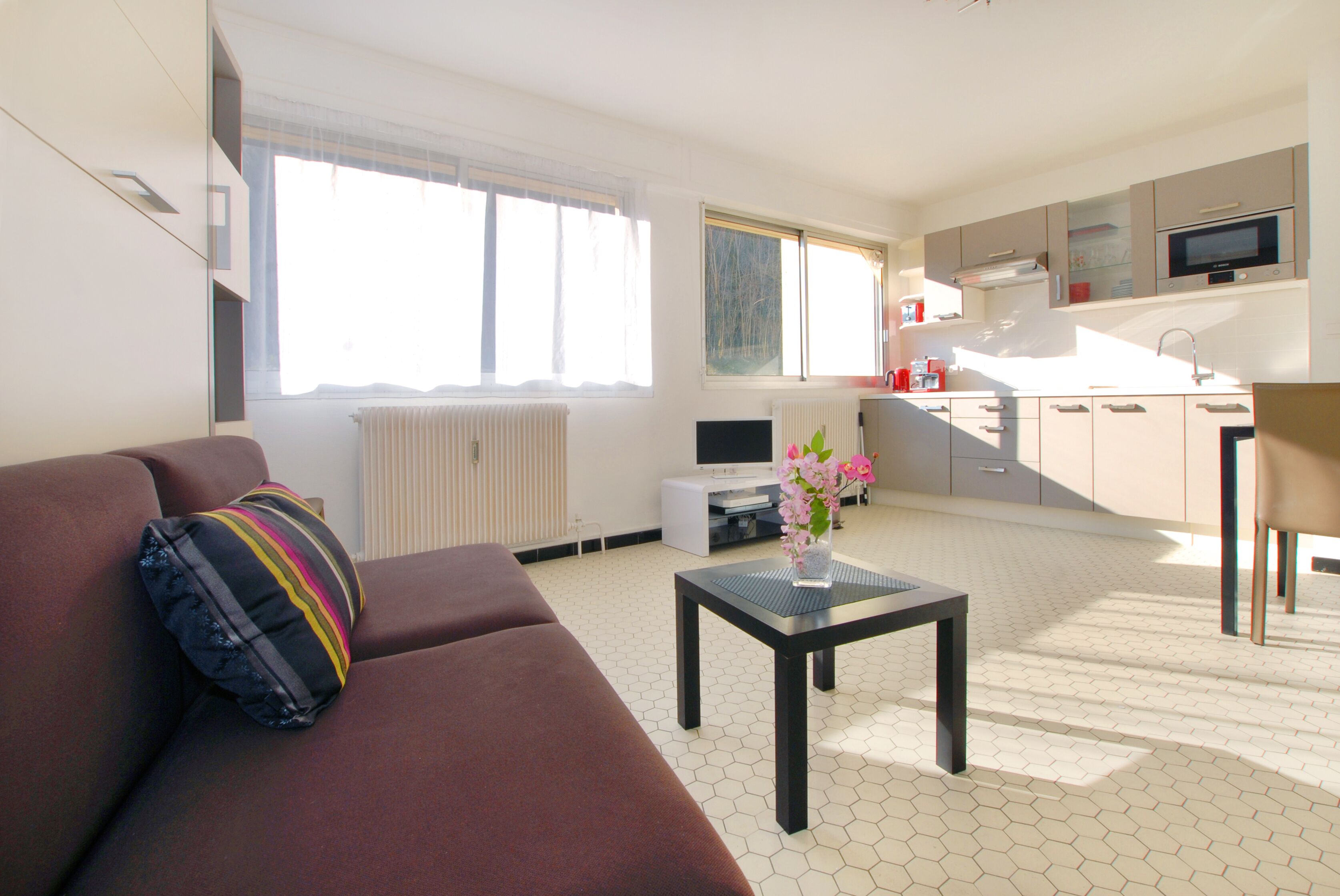 A modern living room with a sofa, a coffee table, and a kitchen area with cabinets and appliances.