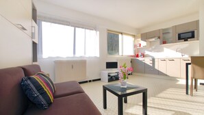 A modern living room with a sofa, a coffee table, and a kitchen area with cabinets and appliances. - Large studio in Valmy, comfort and calm guaranteed (Lyon)