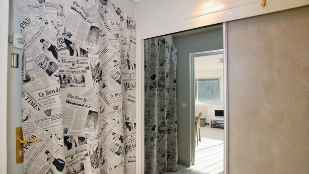 A room with a sliding door covered in newspaper print, a bed, a television, and a small table with a chair. - Large studio in Valmy, comfort and calm guaranteed (Lyon)