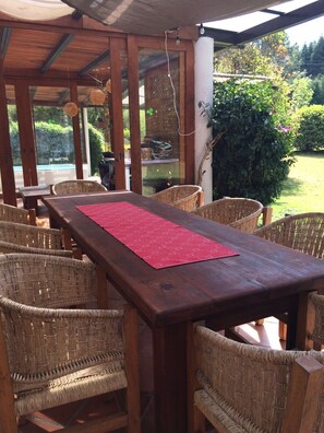An outdoor wooden table with wicker chairs, a red placemat, and a view of a garden and pool. - PEÑA BLANCA EL CIELO RANCHO (AVANDARO)