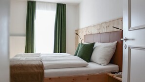 A bedroom with a wooden headboard, a bed with white bedding, green curtains, and a window with blinds. - Deluxe Apartment With Large Balcony, Woodn Interior (Antholz Mittertal)
