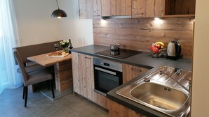 A modern kitchen with wooden cabinets, a built-in oven, a stainless steel sink, and a dining area with a table and chairs. - Deluxe Apartment With Large Balcony, Woodn Interior (Antholz Mittertal)