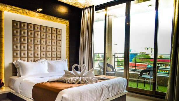 A hotel room with a large bed, a tufted headboard, and a view of a balcony with outdoor seating. - Rudra Shelter International (Vasai)